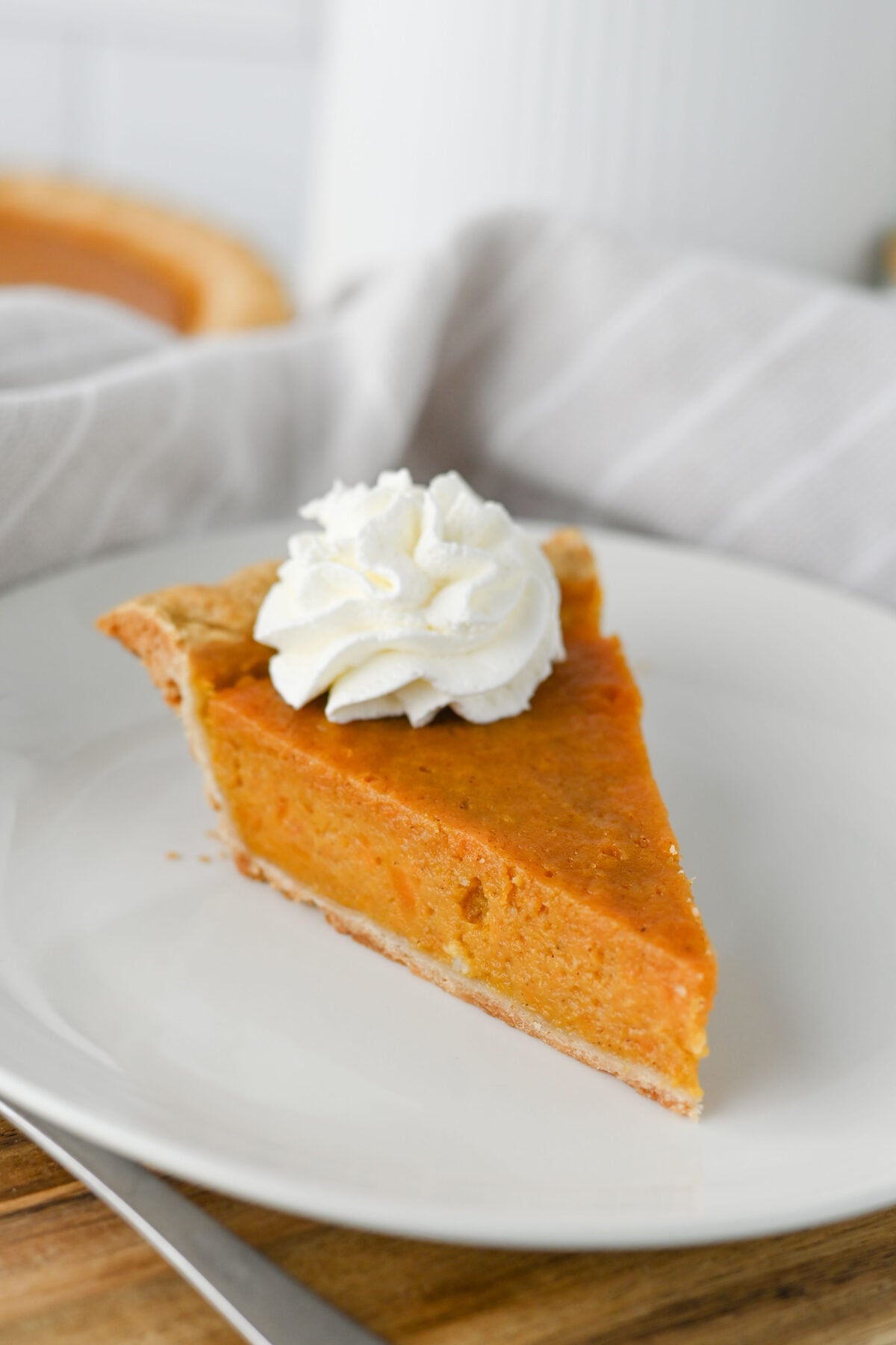 a slice of sweet potato pie with whipped cream on a white plate