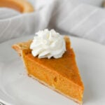 a slice of sweet potato pie with whipped cream on a white plate