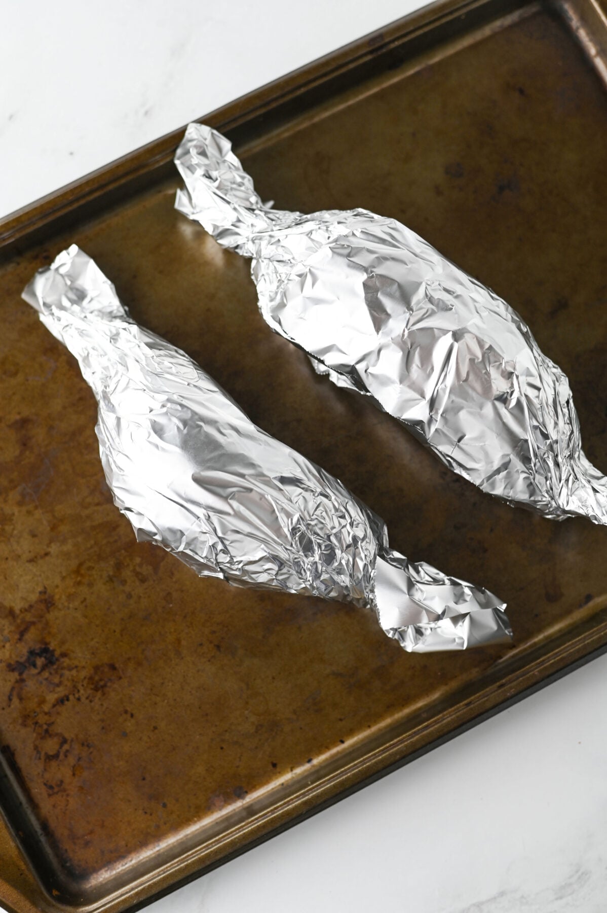 sweet potatoes wrapped in foil on a baking sheet
