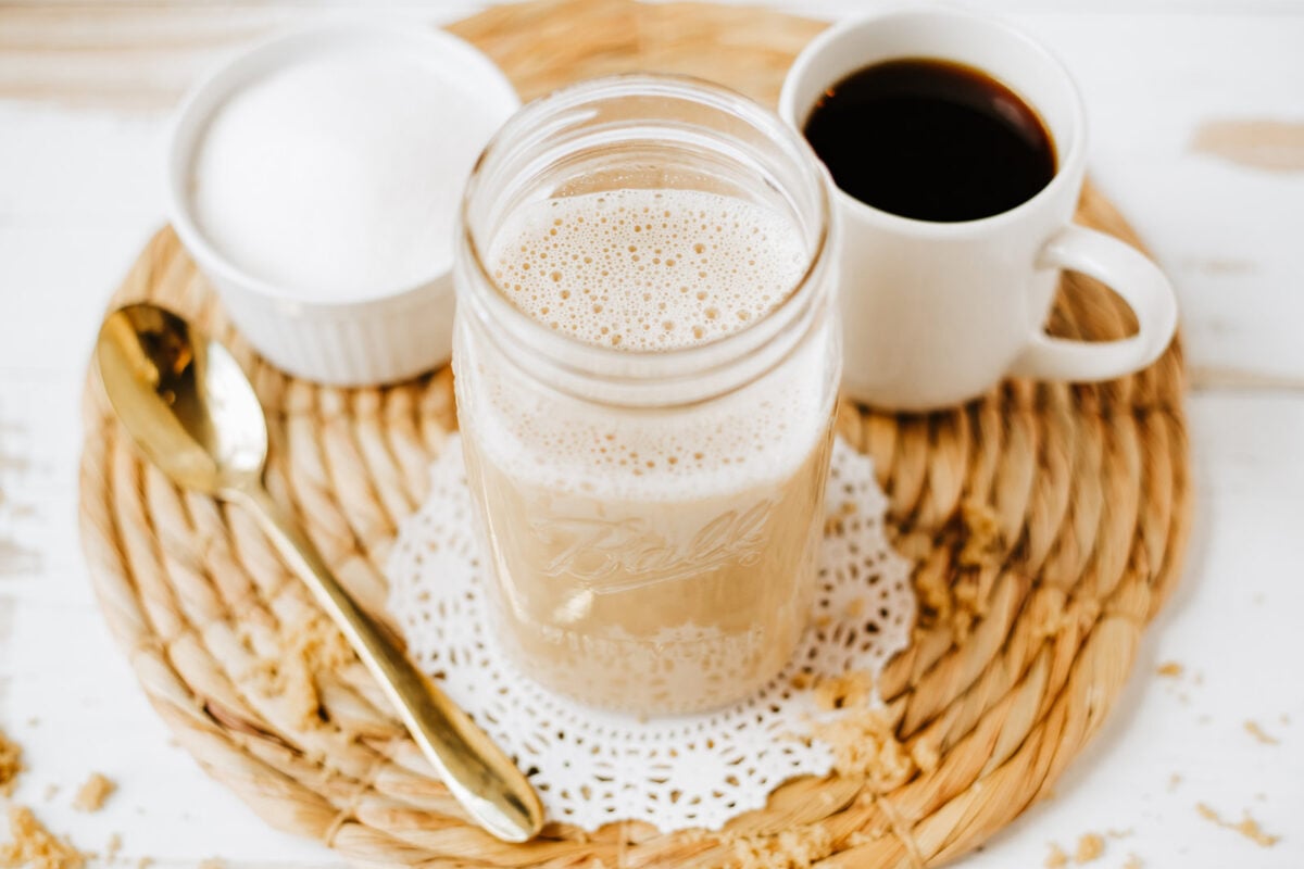 brown sugar coffee creamer in a jar next to a cup of coffee and a bowl of sugar