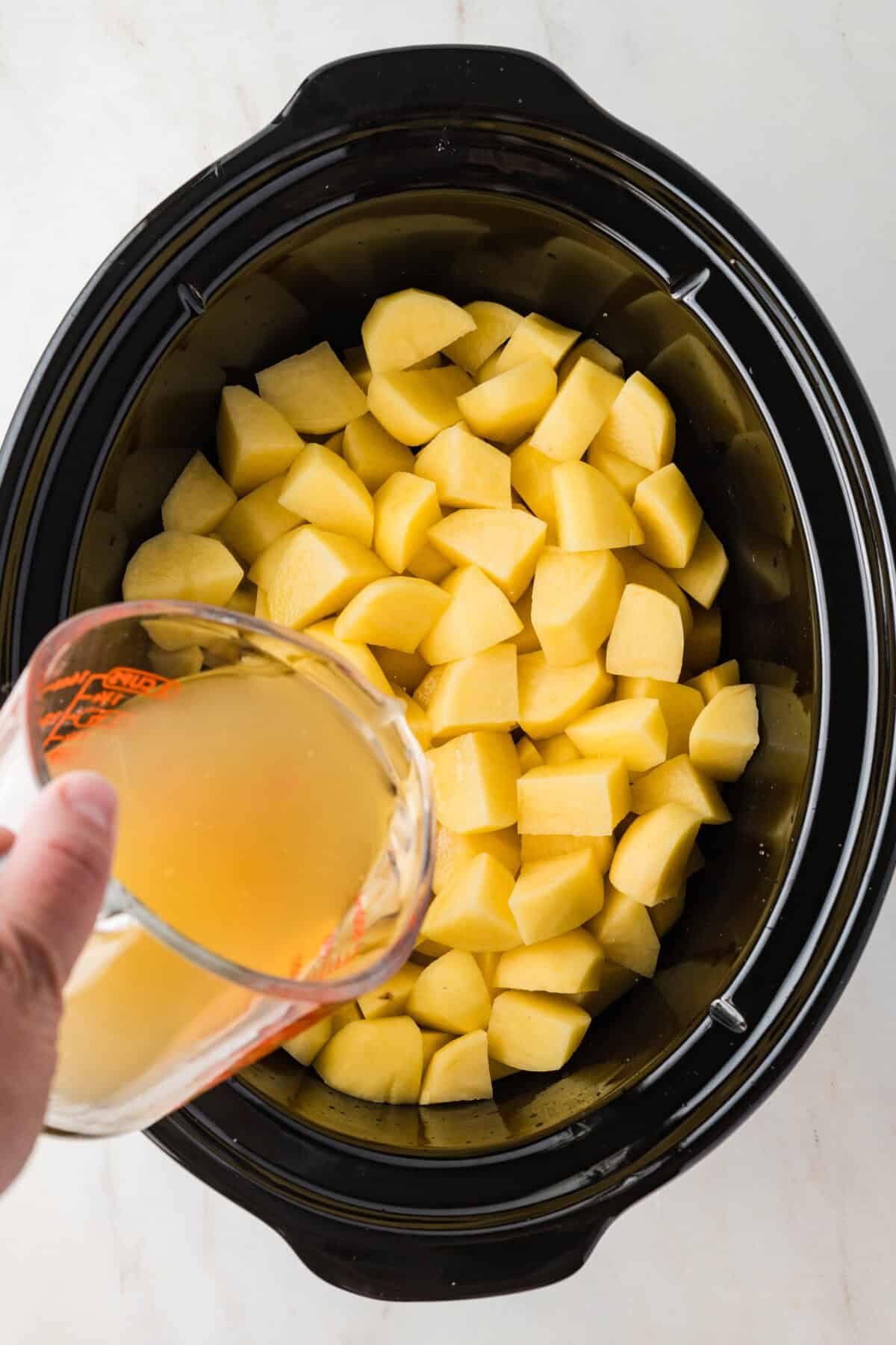 chicken broth being poured over cubed potatoes