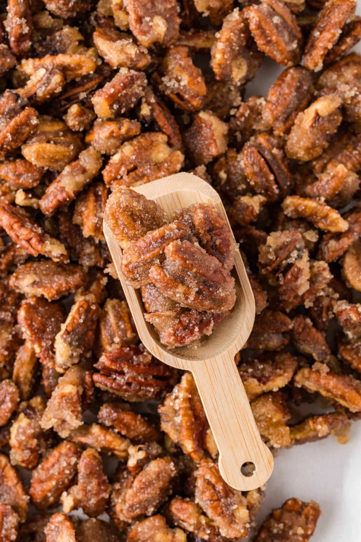 sheet of spiced pecans on a baking sheet with a wooden scoop