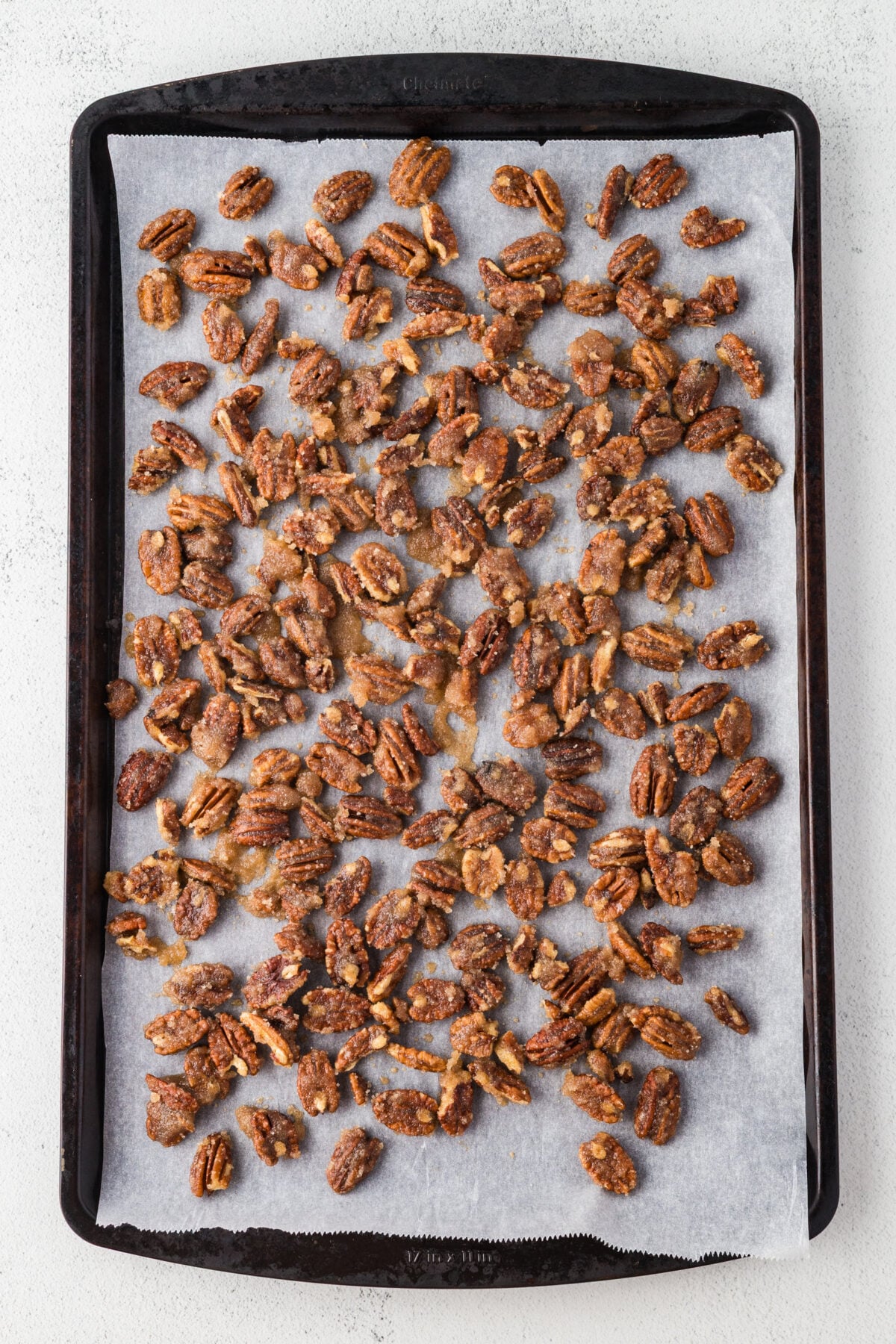 pecans spread out on a baking sheet with parchment paper lining