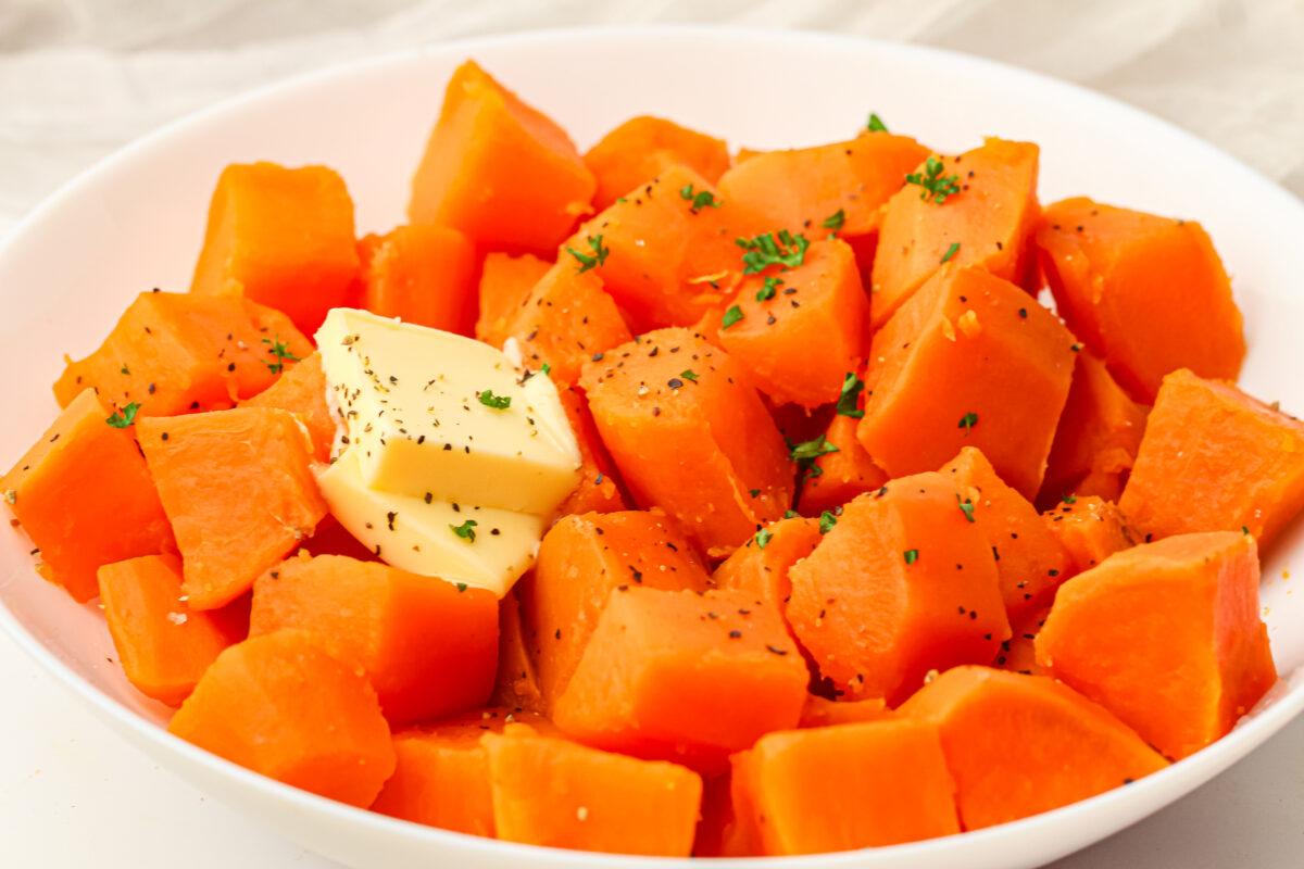 boiled sweet potatoes in a white bowl with butter and parsley