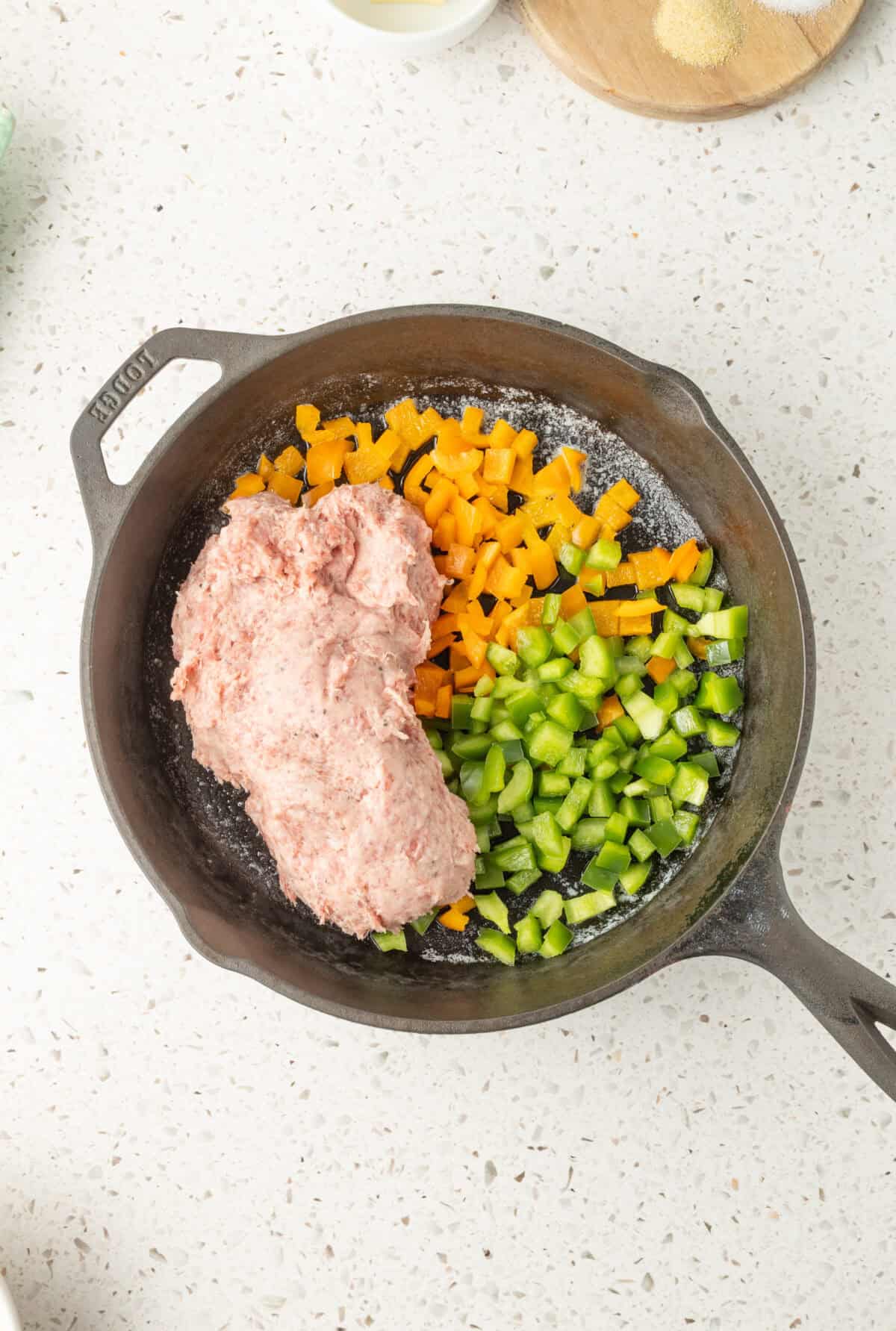raw sausage and veggies in a skillet with butter