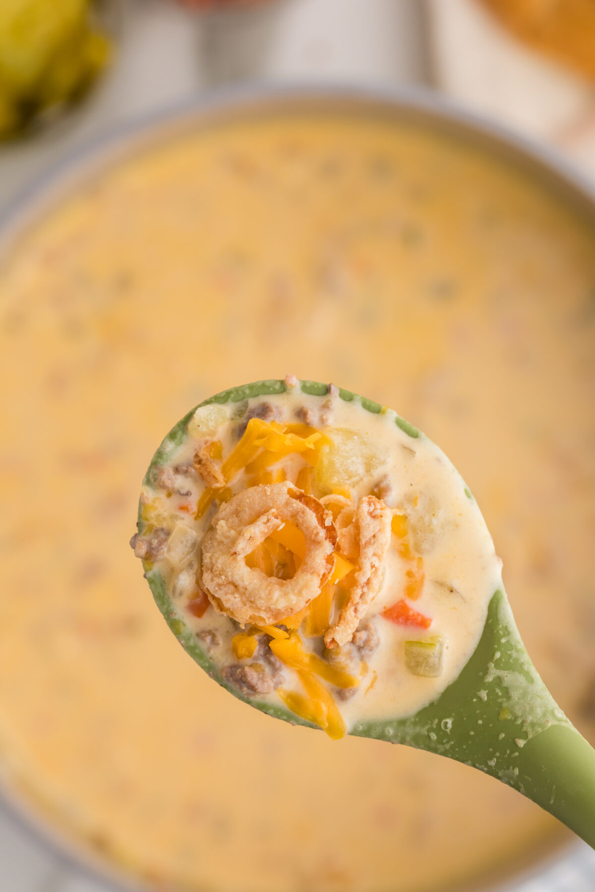 a spoon of cheeseburger soup with crispy onions over the soup pot