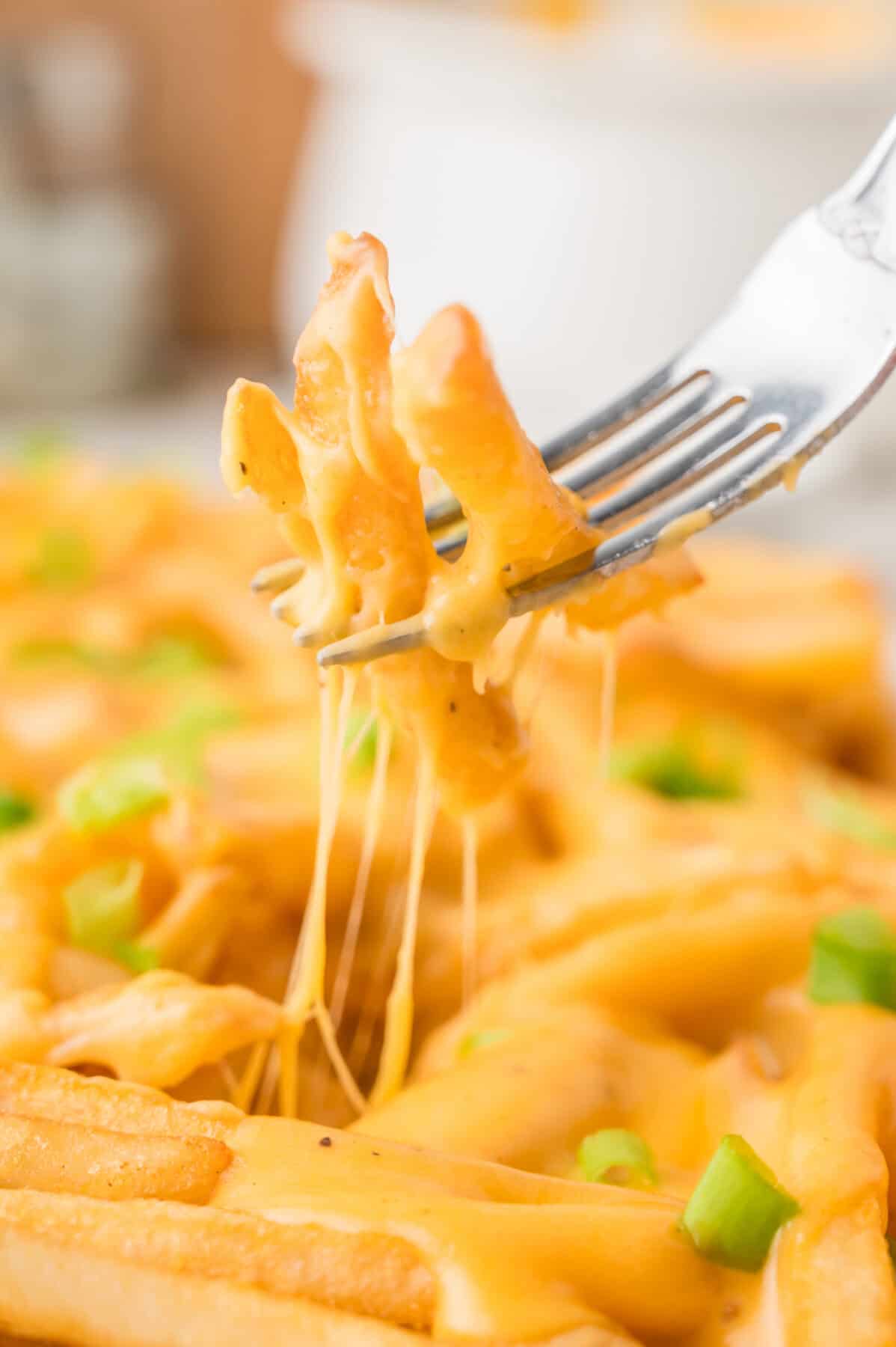 cheese fries on a fork above a pan of fries with cheese pull