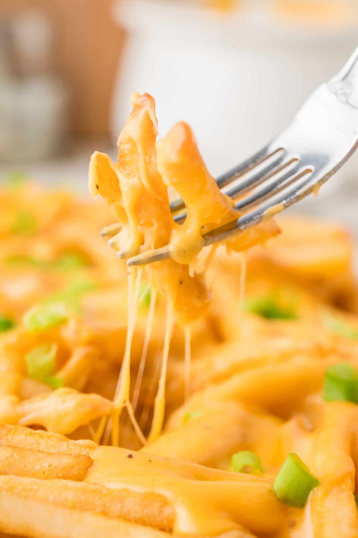 cheese fries on a fork above a pan of fries with cheese pull