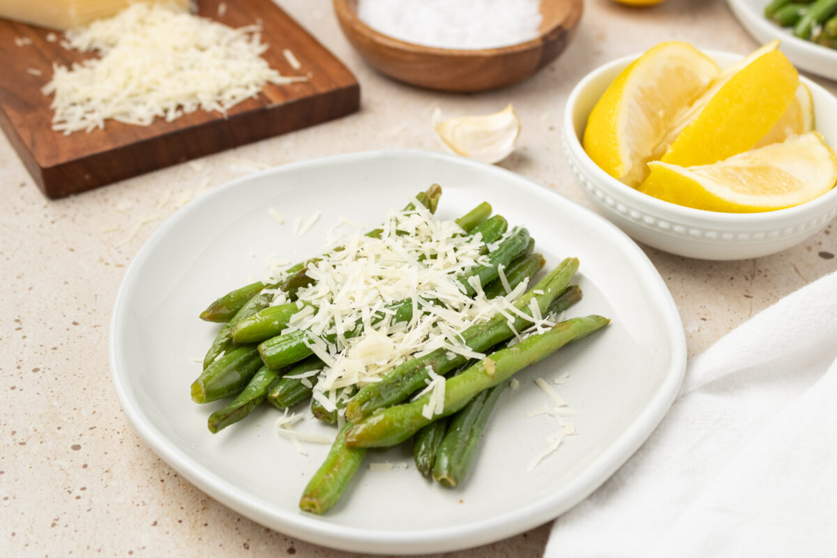 sauteed green beans on a white plate and topped with cheese