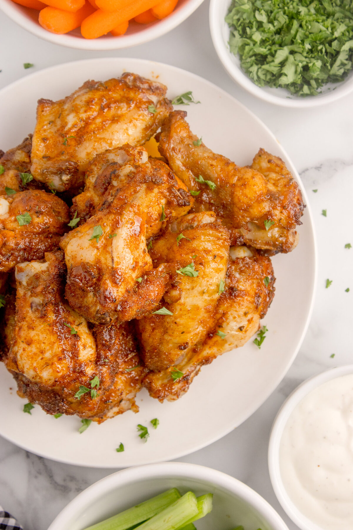 dry rub wings on a plate with bowls of celery, carrots, ranch dressing around it