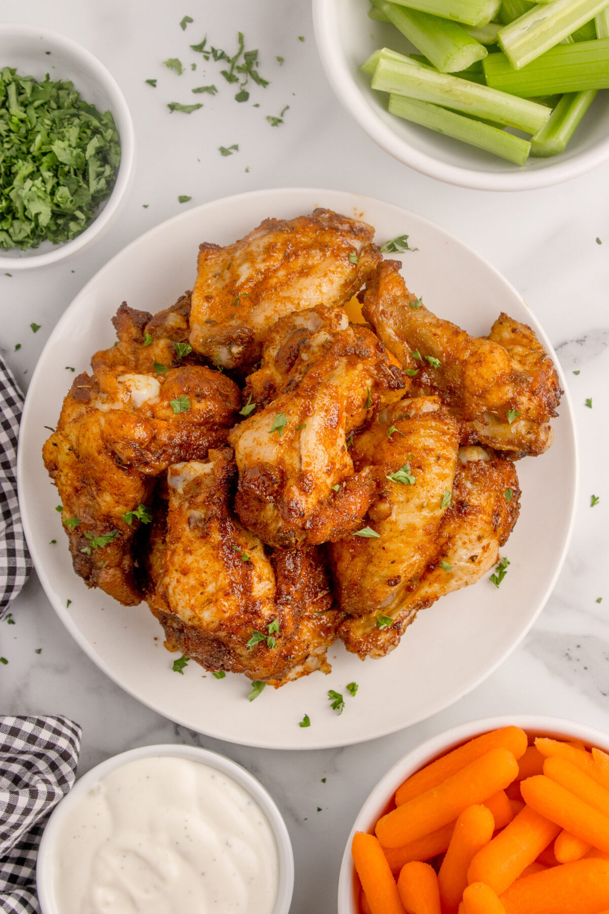 dry rub wings on a plate with bowls of celery, carrots, ranch dressing around it