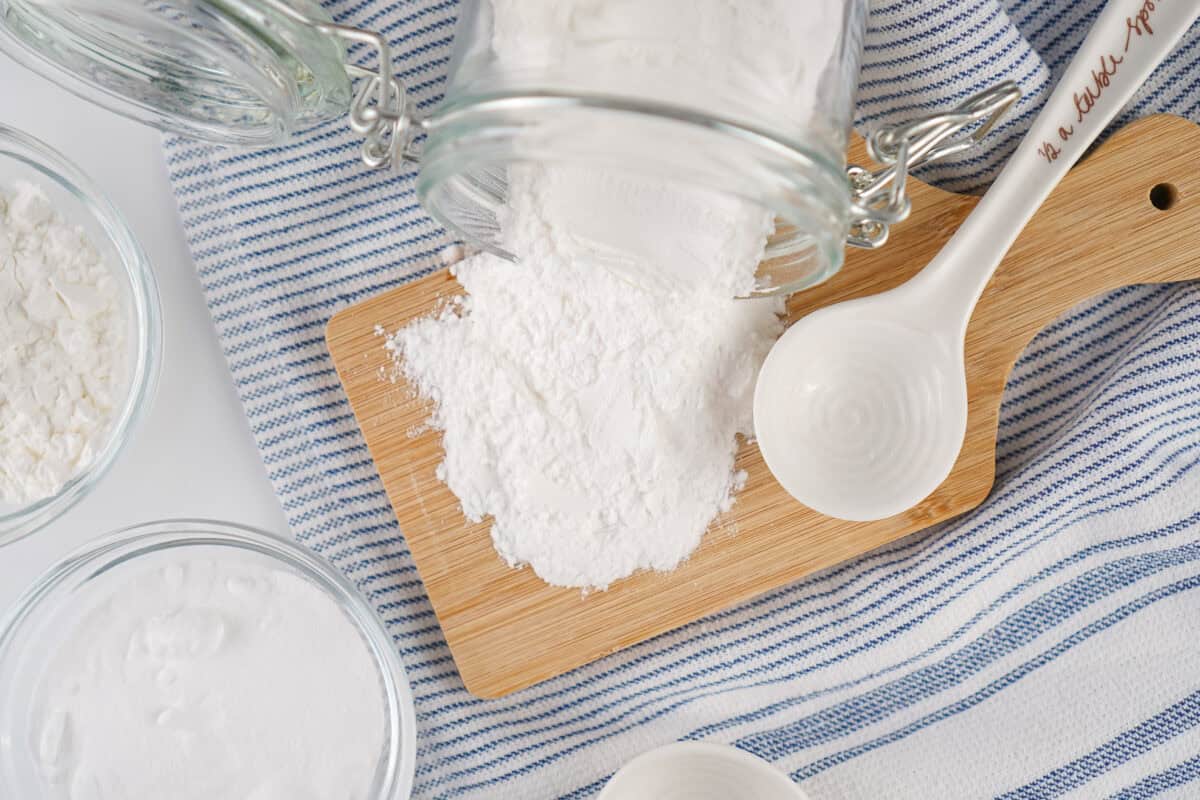 DIY Baking Powder spilling out of jar onto a cutting board next to a spoon