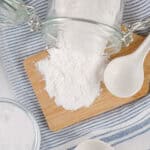 a jar of baking powder spilling onto a cutting board next to a measuring spoon