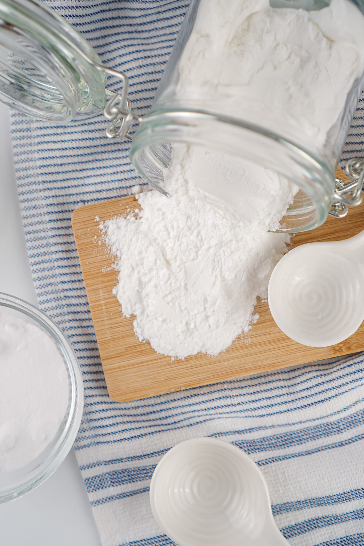 a jar of baking powder spilling onto a cutting board next to a measuring spoon