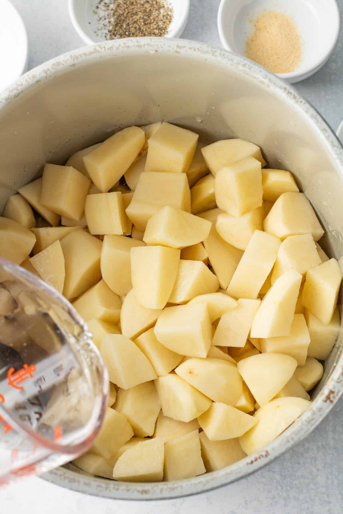 cubed raw potatoes in instant pot with water being poured over
