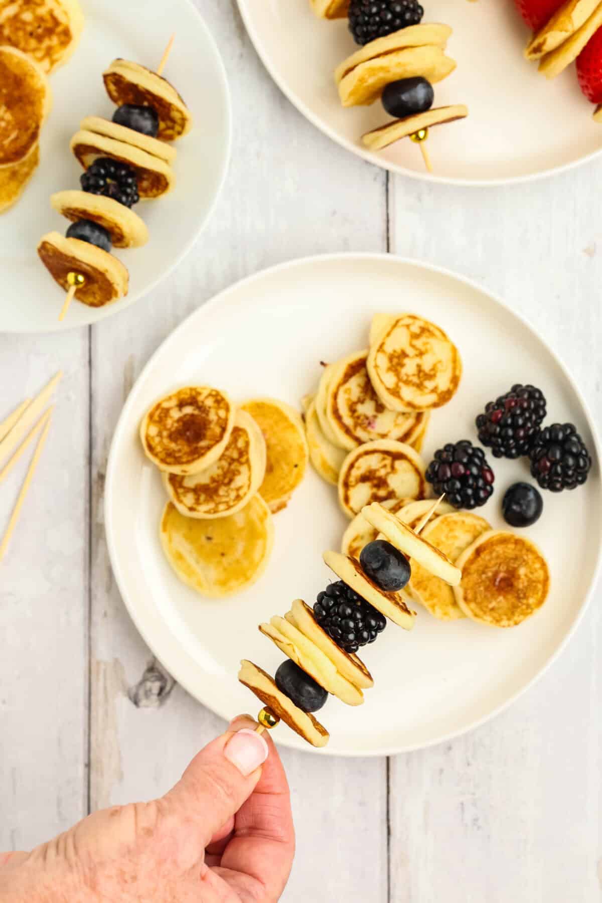 mini pancakes and blackberrie on a plate - with a skewer of pancakes above the plate