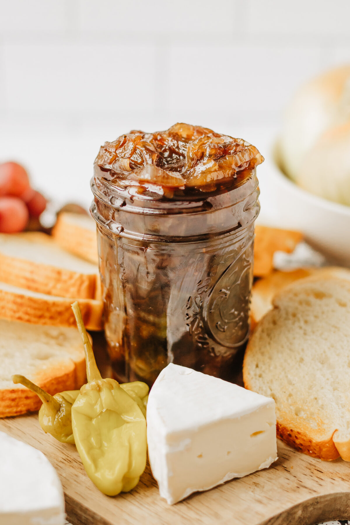 jar of onion jam next to pepper and cheese and bread on a cutting board