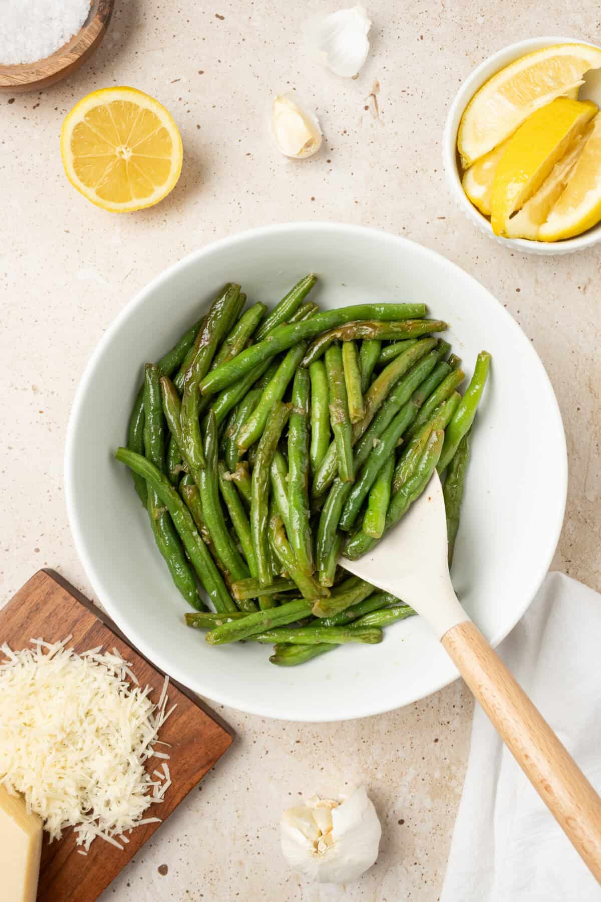 sauteed green beans in a white bowl with a wooden spoon