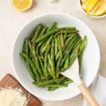 sauteed green beans in a white bowl with a wooden spoon